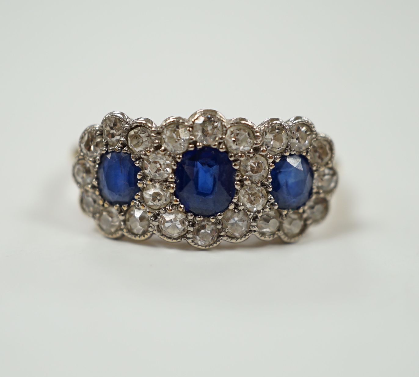 A yellow metal and millegrain set sapphire and diamond triple cluster ring, size K/L, gross weight 2.5 grams.